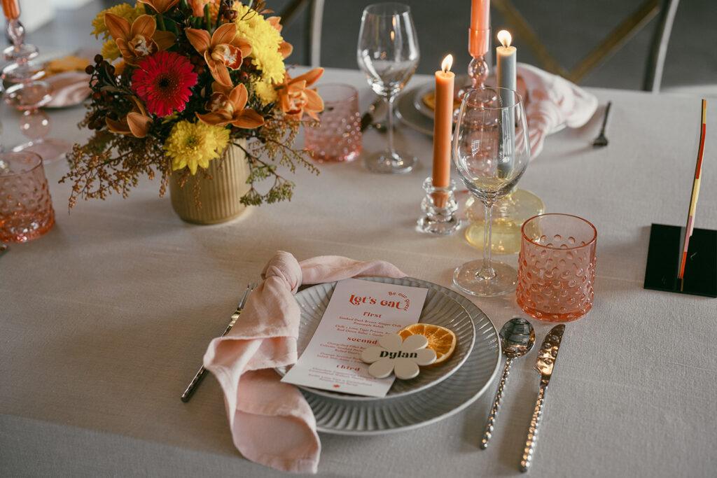 Retro tablescape showing the florals with pops of pink, yellow and orange, colourful candles lit in background