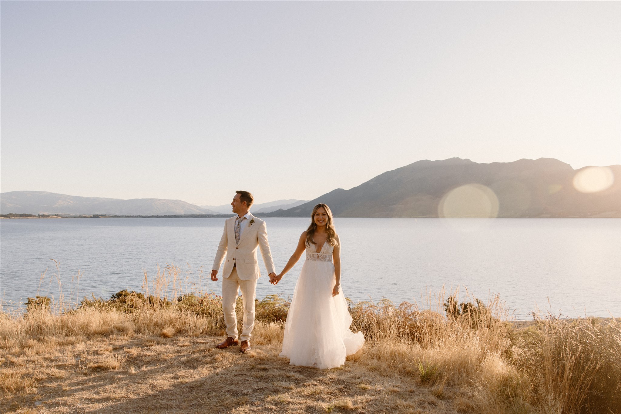 Bride and groom holding hands in the golden hour with lake wanaka and the mountains in the background