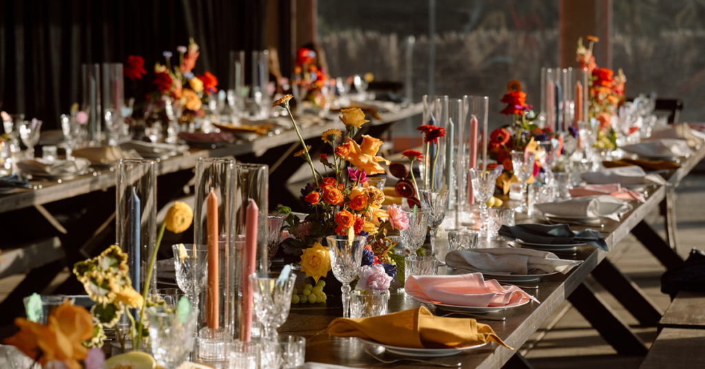 Colourful wedding table scape with lots of yellow, orange and red florals, colourful tall candles and crystal glasses. Set on dark wood, long tables